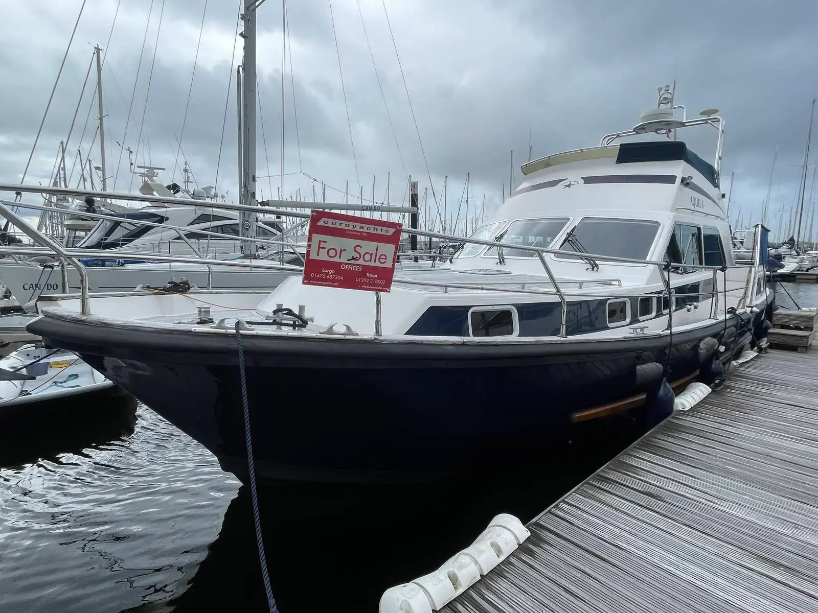 Aquastar 48 S: navy hull and white superstructure seen from the bow, moored alongside a marina pontoon