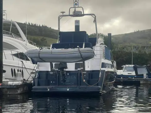 Aquastar 48 S: stern view showing tender on davits, bathing platform and flybridge arch in a wooded marina
