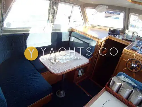 Aquastar Pacesetter 27 Boat For Sale: saloon with blue C-shaped seating around a table, wheel and helm instruments to starboard