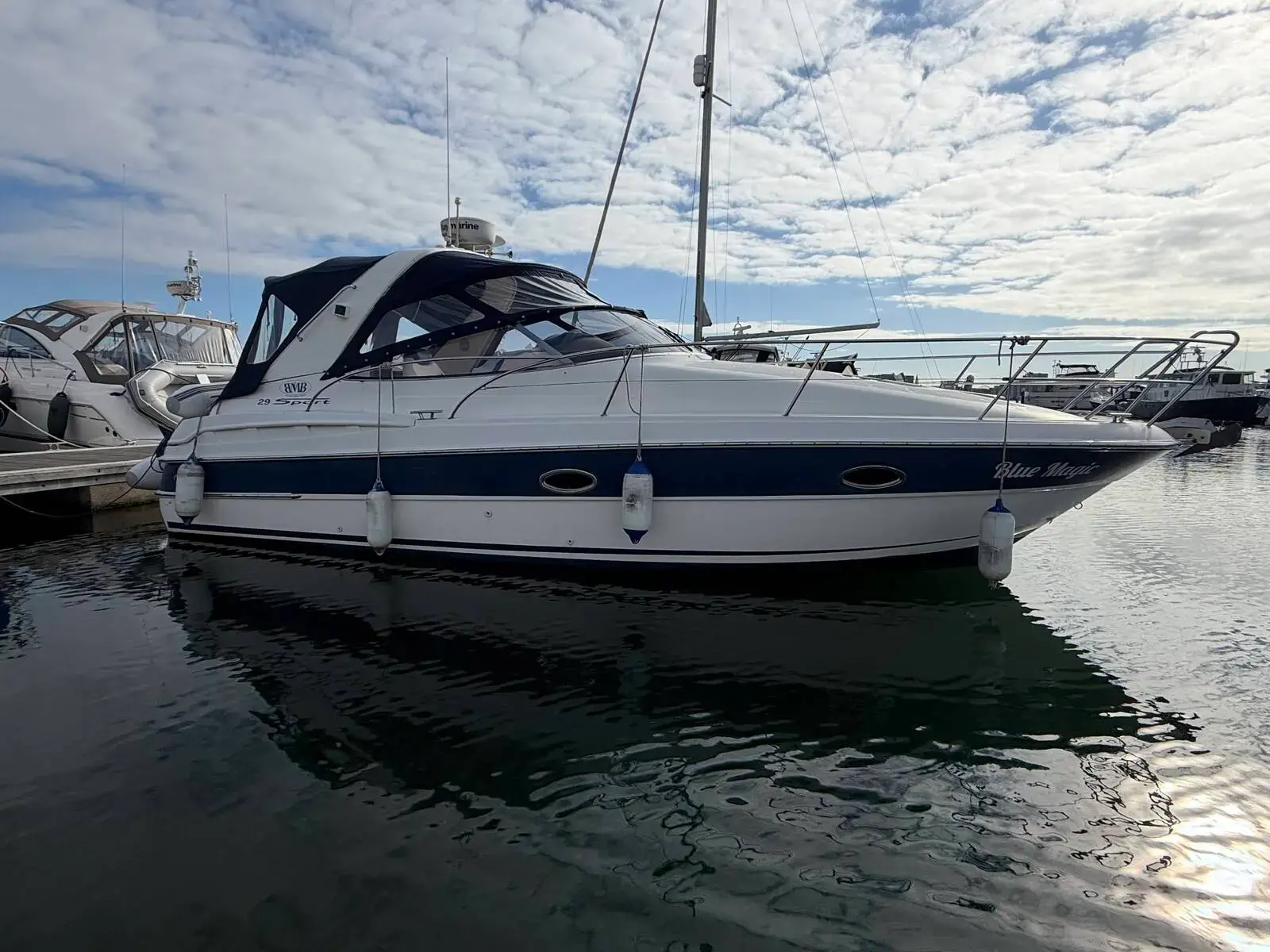 Bavaria 29 Sport: white hull with navy stripe moored in a marina, dark canvas enclosure over the cockpit