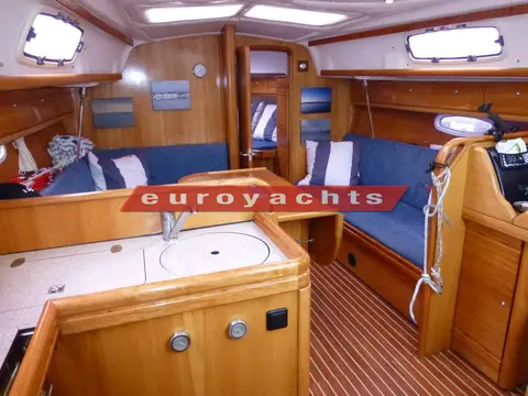 Bavaria 33 Cruiser: saloon with blue upholstery, warm wood joinery and galley sink in foreground