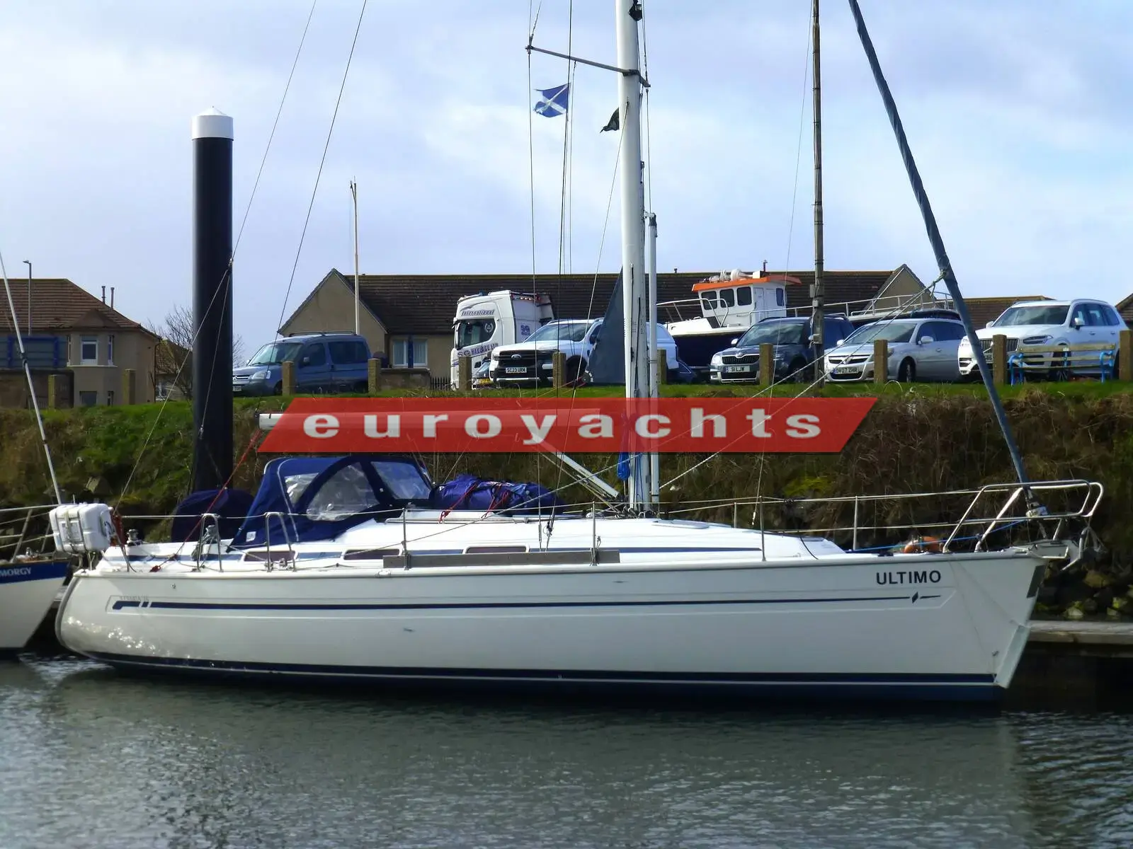 Bavaria 36: white hull moored alongside a pontoon with blue sprayhood and houses behind