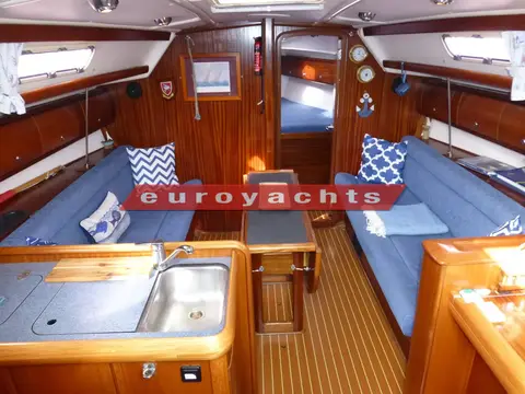Bavaria 36: saloon looking forward with blue settees, central dining table and galley sinks in foreground