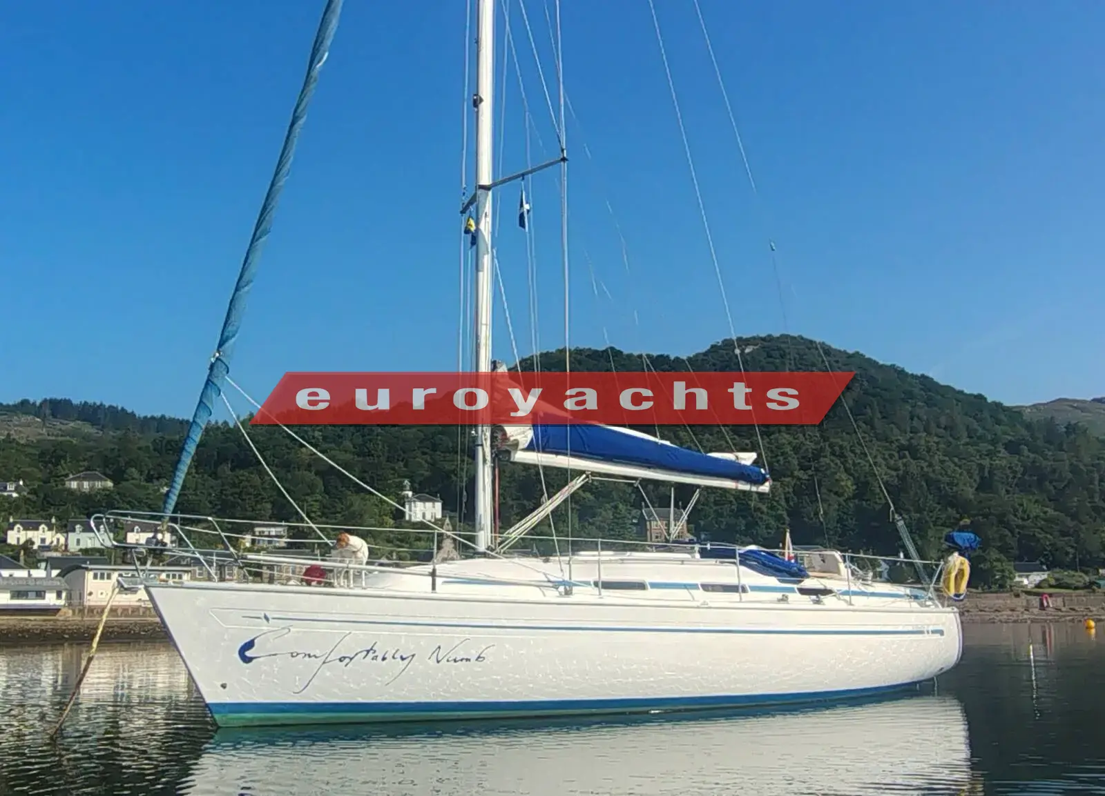 Bavaria 37: white hull with blue sail cover at anchor beneath green hills on a clear day