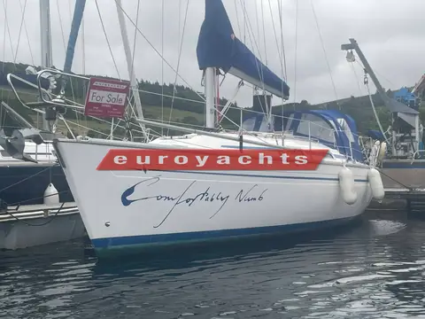 Bavaria 37: hull and blue sprayhood afloat in a marina with hillside behind