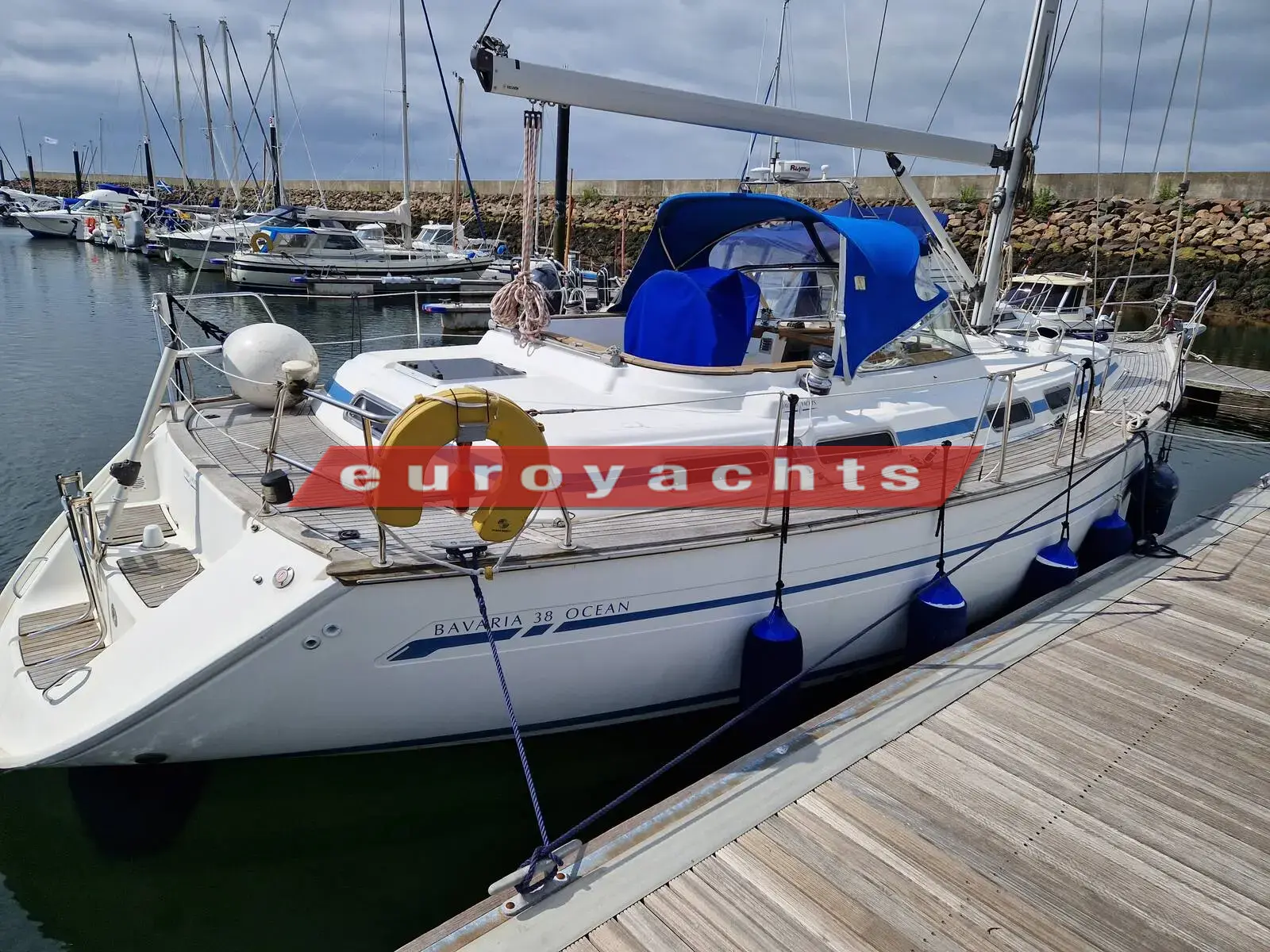 Bavaria 38 Ocean: port side of the white hull moored alongside a pontoon, blue sprayhood and lifebuoy on the rail