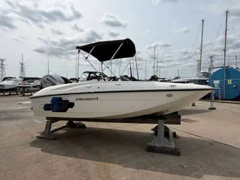 Bayliner 160 Element: port side view of hull on stands with bimini raised, marina behind
