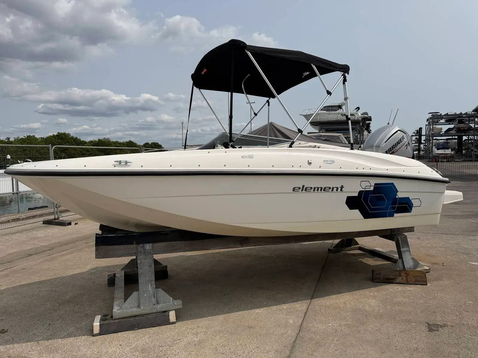 Bayliner 160 Element: starboard side of white bowrider hull with black bimini, ashore on stands