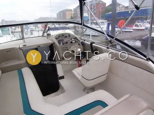 Bayliner 2655 Ciera: cockpit with cream upholstery and teal trim, pilot seat, helm and open cabin door