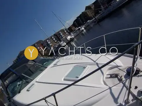 Bayliner 285: white foredeck with hatch, rails and anchor windlass, apartment blocks beyond