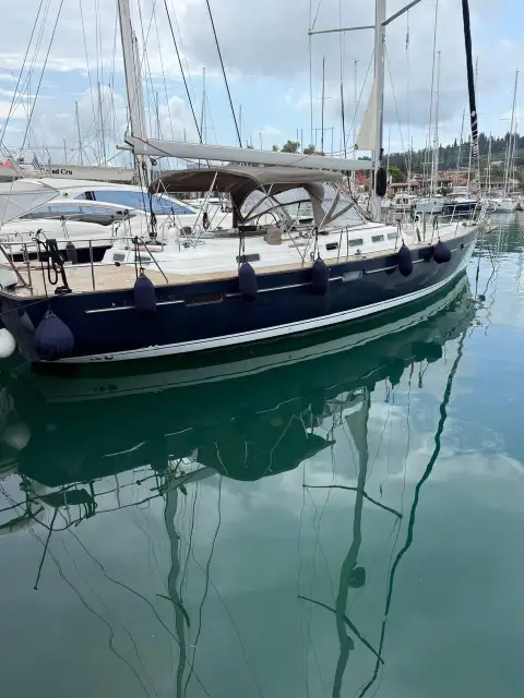Beneteau 57: dark blue topsides reflected in calm marina water, bimini fitted over centre cockpit