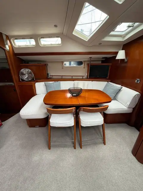 Beneteau 57: saloon dining table with two white chairs, wraparound settee and overhead hatches