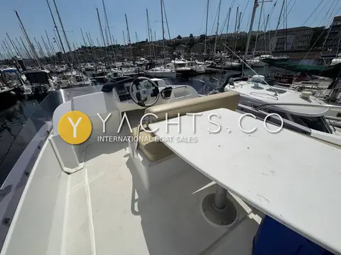 Beneteau Antares 30: flybridge with white table, helm seat and marina view on a sunny day