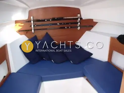 Beneteau Antares 6: forward saloon with blue upholstered seating, navy cushions and fishing rods racked on wood panel