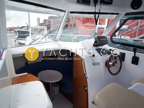 Beneteau Antares 7: wheelhouse with navy curved saloon seating, round table, wooden wheel and Raymarine instruments