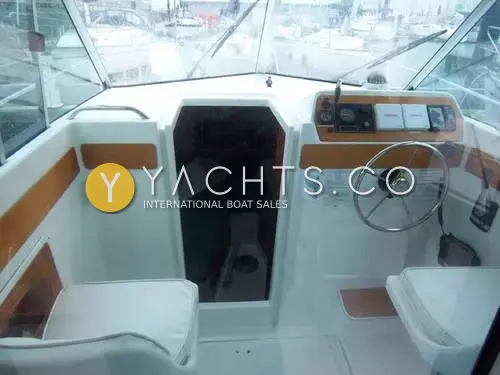 Beneteau Antares 7: wheelhouse looking forward, helm with wood-trimmed console, white seats and open door to cabin