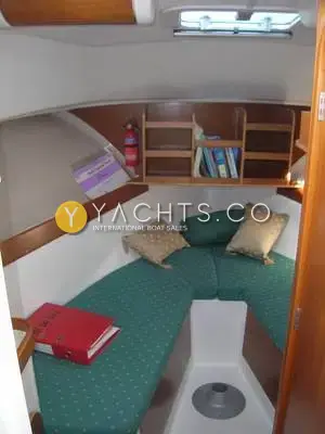 Beneteau Antares 7: forward cabin with green upholstered V berth, wooden bookshelf and fire extinguisher
