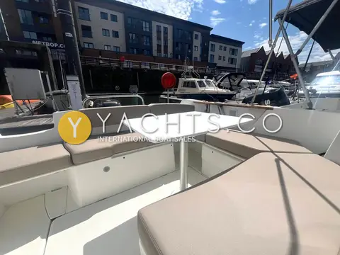 Beneteau Antares 7.80: cockpit seating with grey cushions around a white table, apartments behind