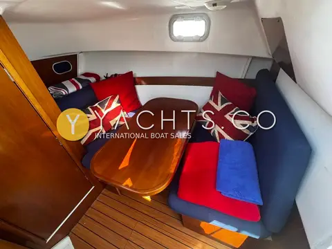 Beneteau Antares 710: lower saloon with wooden table and blue seating dressed with Union Jack cushions