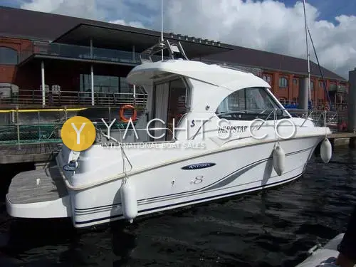 Beneteau Antares 8: starboard side of the white hull moored in a marina, with a teak bathing platform and fenders out