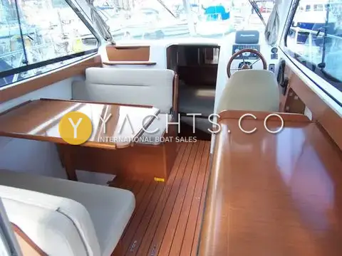 Beneteau Antares 8: wheelhouse interior with dinette table, light upholstery, wood-effect floor and helm seat forward