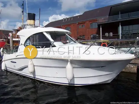 Beneteau Antares 8: bow quarter view of the white hull and wheelhouse beside a brick quayside building