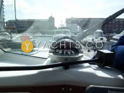 Beneteau Antares 9: helm compass on the dashboard with marina buildings beyond the windscreen