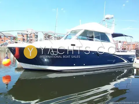 Beneteau Antares 9: starboard side profile showing navy blue hull and radar arch, reflected in calm marina water