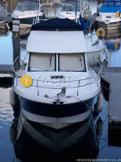 Beneteau Antares 9.80 Anniversary Edition: bow view of the boat moored on a pontoon with flybridge covered in navy canvas