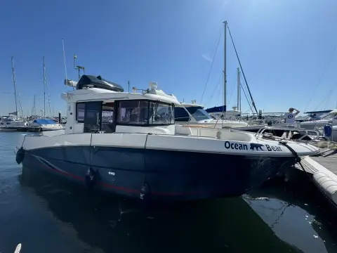 Beneteau Barracuda 9: starboard bow view of the dark hull and wheelhouse in a sunny marina