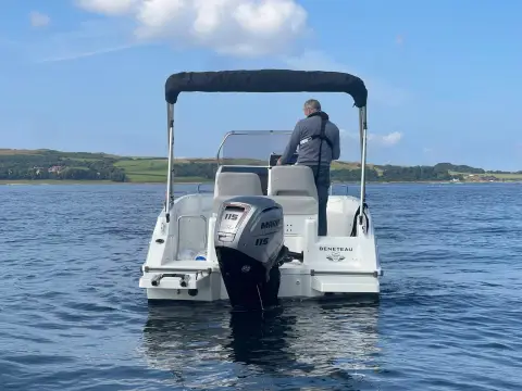 Beneteau Flyer 6 Space Deck: stern view showing the outboard engine, bimini and helm seats, with green shoreline behind