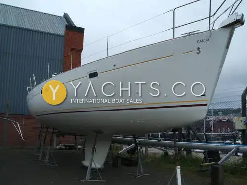 Beneteau Oceanis 411 Clipper: white hull ashore on stands in a boatyard, showing gold and red cove stripes and keel