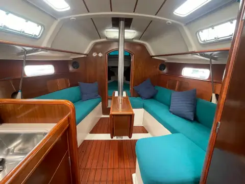 Beneteau Oceanis Clipper 321: saloon looking forward with teal U-shaped seating, cherry wood joinery and central table