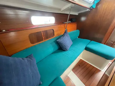 Beneteau Oceanis Clipper 321: saloon seating in teal upholstery beneath a hull portlight and wood shelving