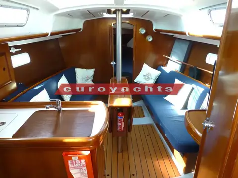Beneteau Oceanis Clipper 323: saloon looking forward with blue settees, wood joinery and central drop-leaf table