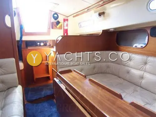Contessa 32: saloon looking aft to companionway steps, cream buttoned upholstery and folding wooden table