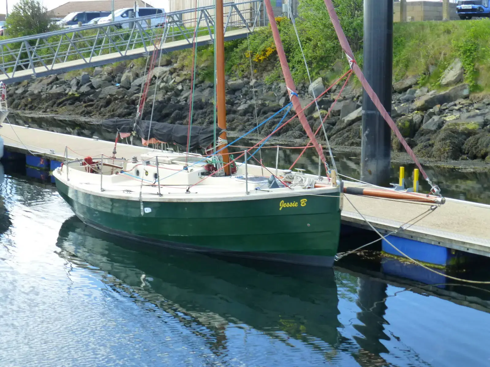Cornish Crabber 22 Gaff Cutter: dark green hull with cream deck moored alongside a pontoon by a rocky harbour wall