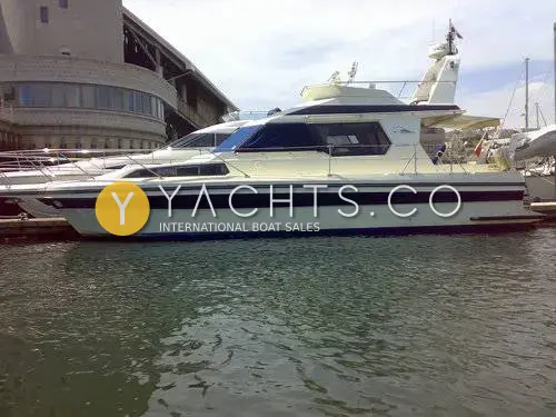 Cougar Advance 41 Boat For Sale: starboard side of the white hull with navy stripes and flybridge, moored beside a curved building