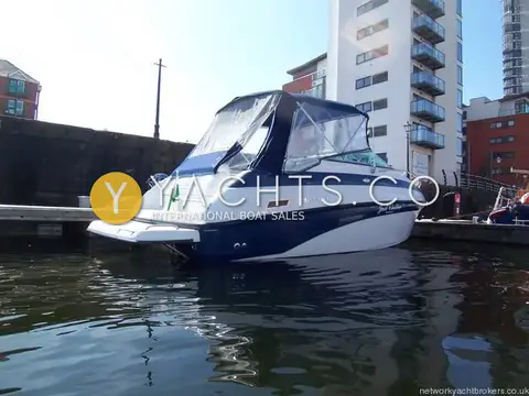 Crownline 230 CCR: starboard quarter view showing navy canopy and blue hull beside tall marina apartments