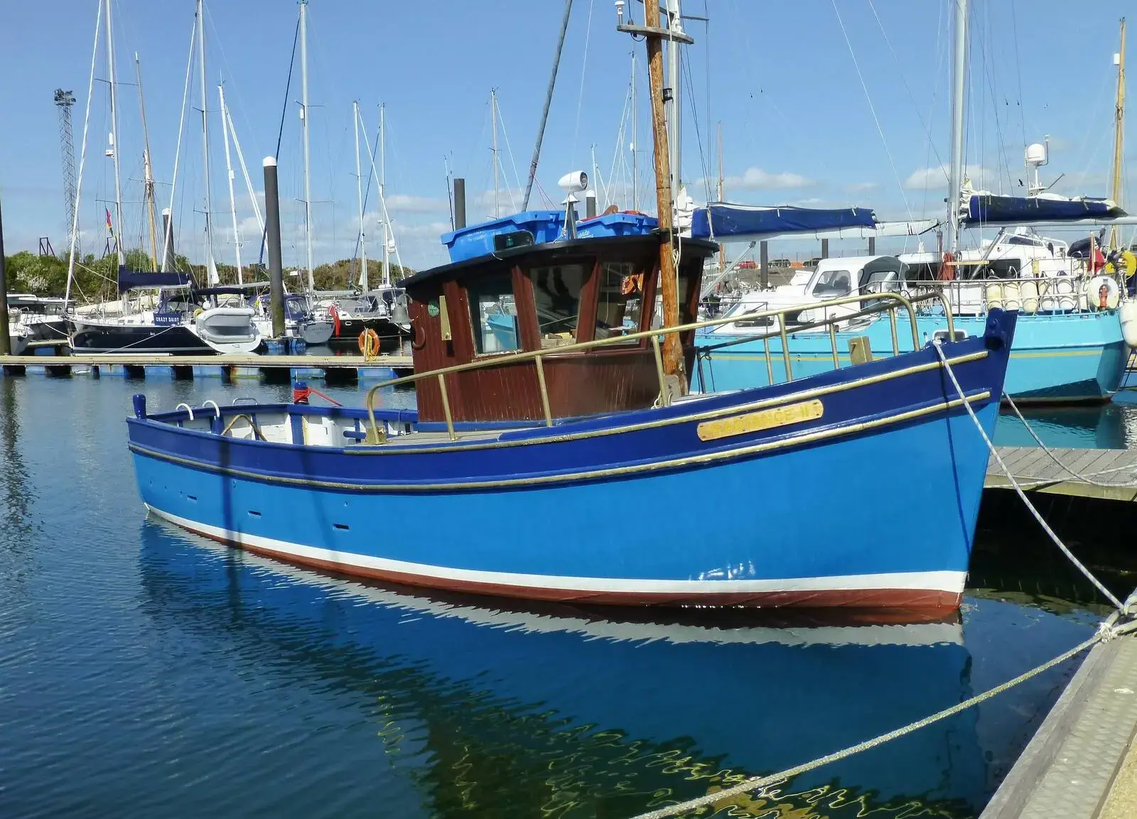 Custom Built John Gaff 8.25 Fishing Boat: blue wooden hull with varnished wheelhouse and wooden mast, afloat in a marina