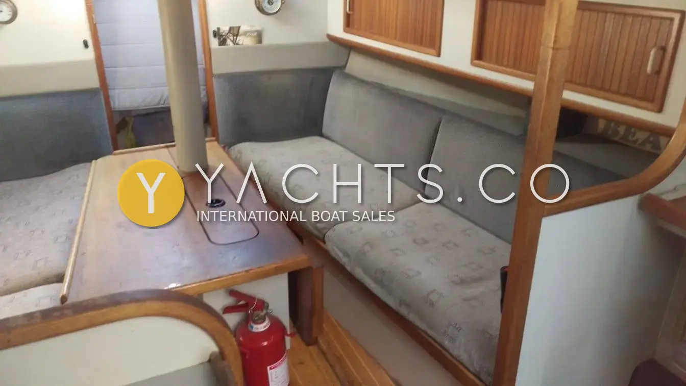 Dehler 34 Top Nova: saloon with grey patterned settee, wooden table around the mast support and fire extinguisher