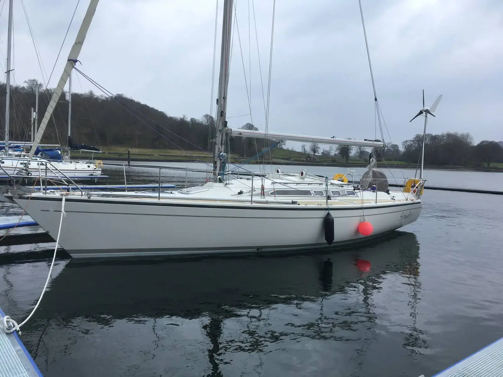 Dehler 38 CWS: starboard side afloat in a marina on a grey day, wind generator on stern arch