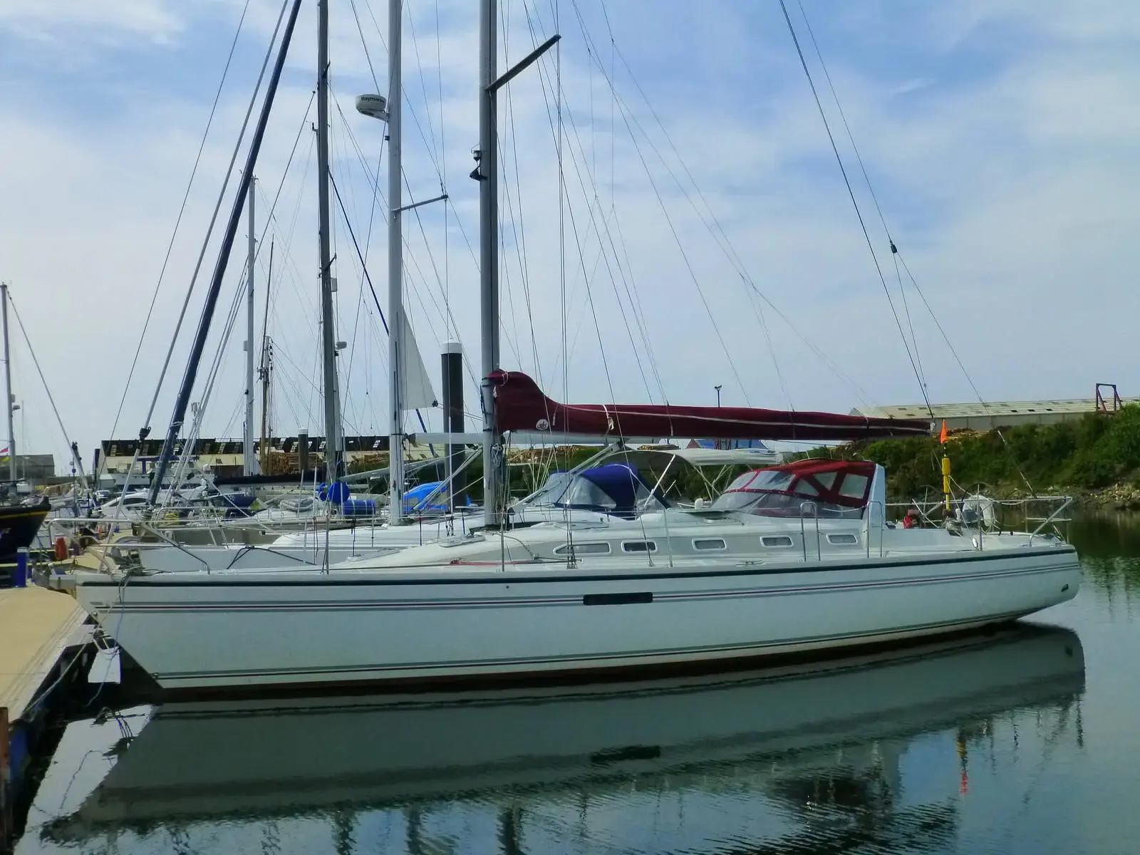 Dehler 43 CWS: white-hulled sloop moored stern-on in a marina, with a red sail cover on the boom