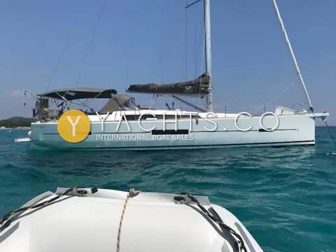 Dufour 520 Grand Large: port side profile at anchor with bimini, sprayhood and covered mainsail, wooded shore behind