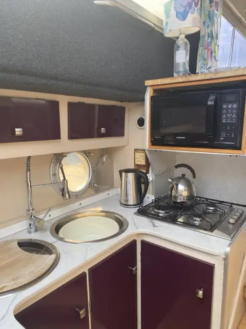 Fairline 40: galley with white worktops, round sink, gas hob, microwave and burgundy cupboard doors
