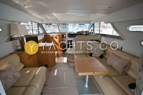 Fairline Phantom 41: saloon with cream leather seating, wooden table and lower helm ahead under wraparound windows
