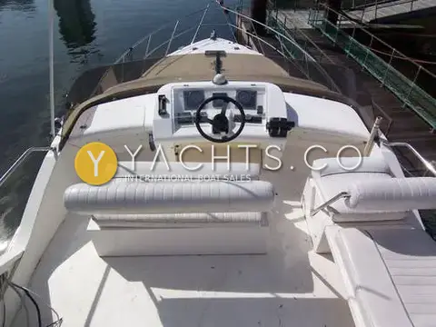 Fairline Phantom 41 Reduced: flybridge helm with white bench seating and helm seat, moored alongside a pontoon
