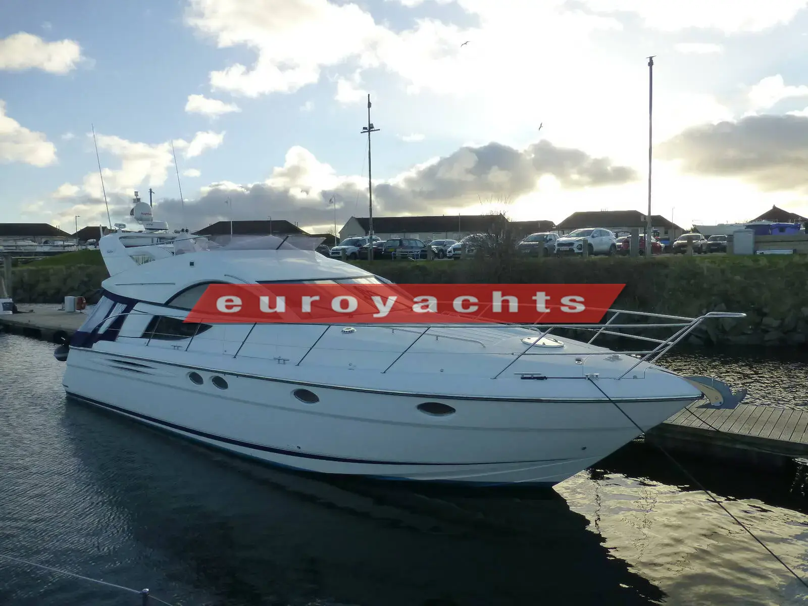 Fairline Phantom 46: white flybridge motor cruiser moored alongside a quiet pontoon under a cloudy sky