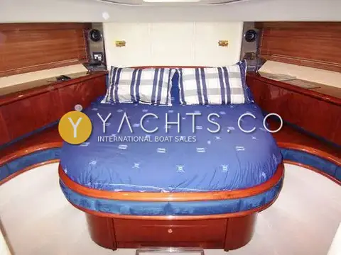 Fairline Squadron 58: forward master cabin with central double berth in blue bedding and cherry side lockers