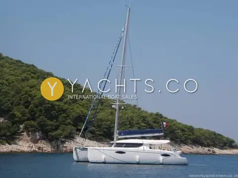 Fountaine Pajot Orana 44: profile at anchor off a wooded rocky shore, flying a French ensign